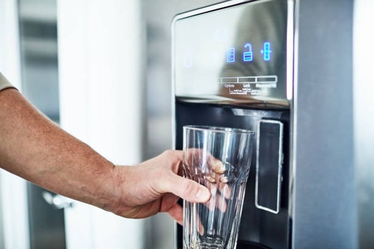 Person filling a glass with water from a refrigerator water dispenser.