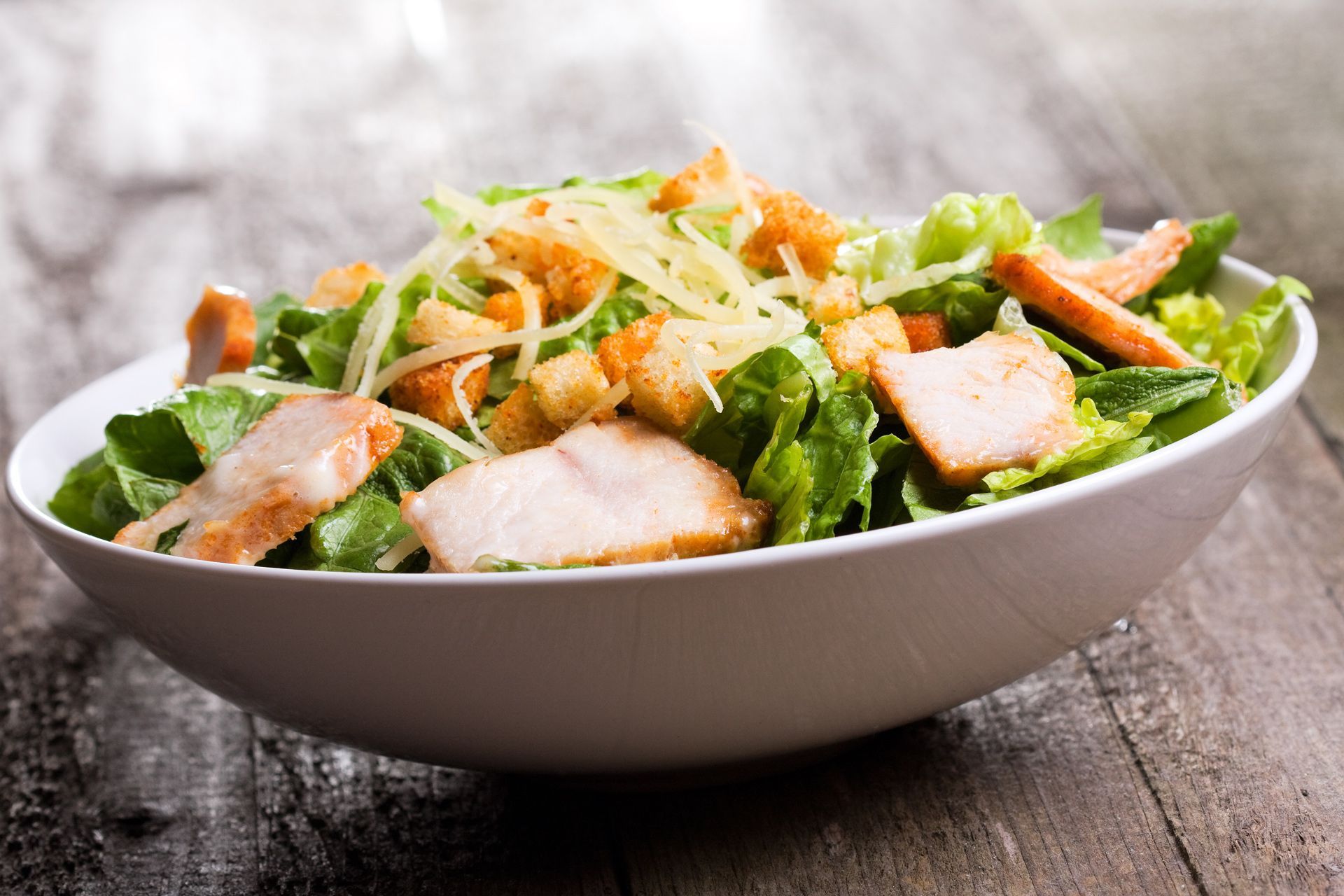 Chicken Caesar salad in a white bowl on a wooden surface.
