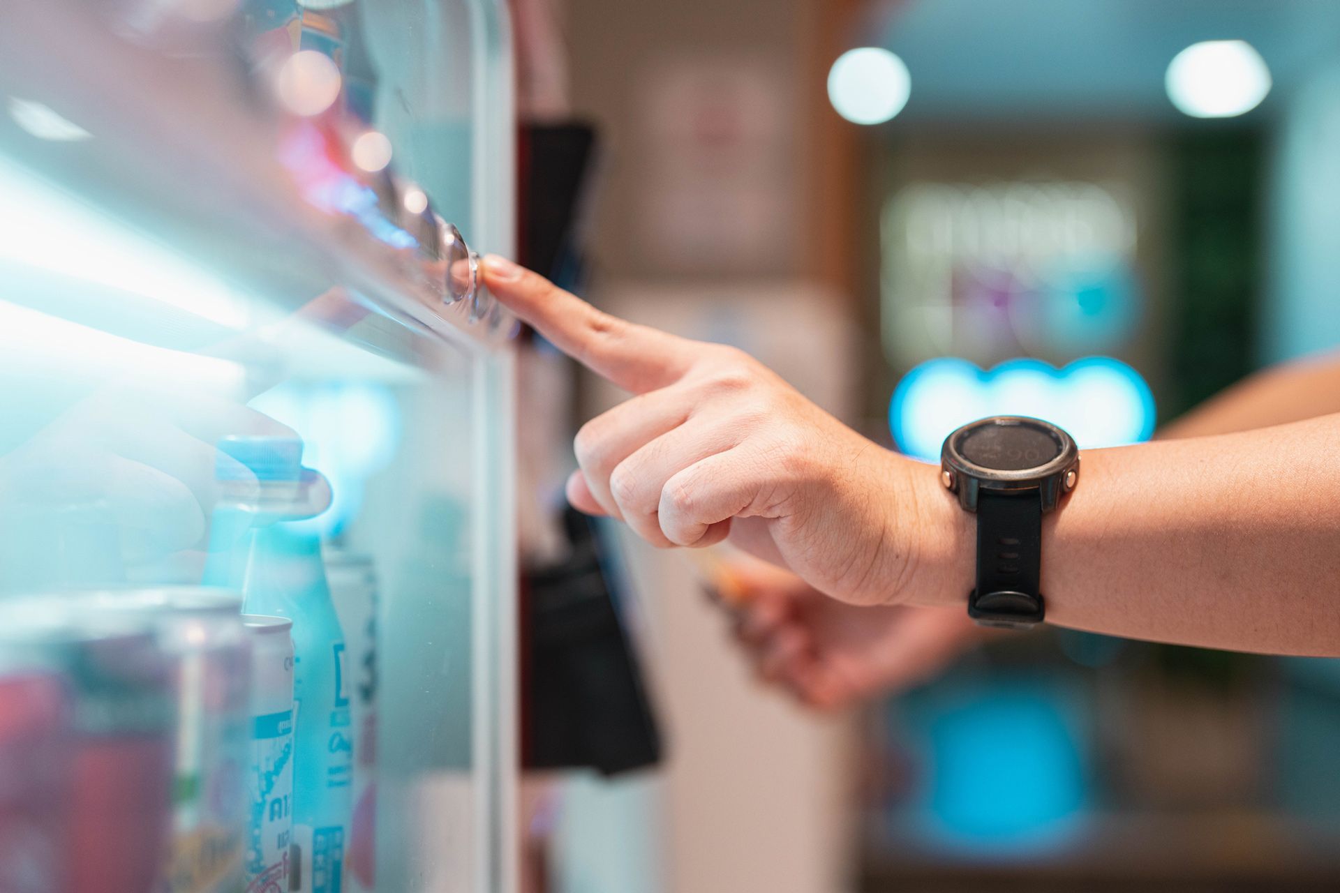 Hand with smartwatch pressing a vending machine button, selecting a drink.