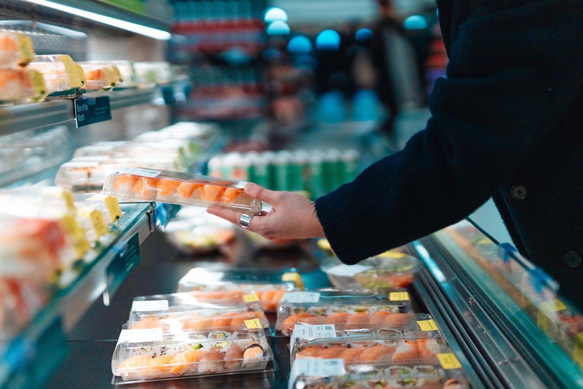 Person reaching for a sushi roll in a refrigerated grocery display case.