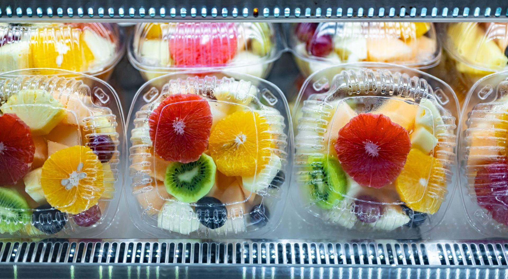 Fruit salads in clear plastic containers displayed in a refrigerated case.