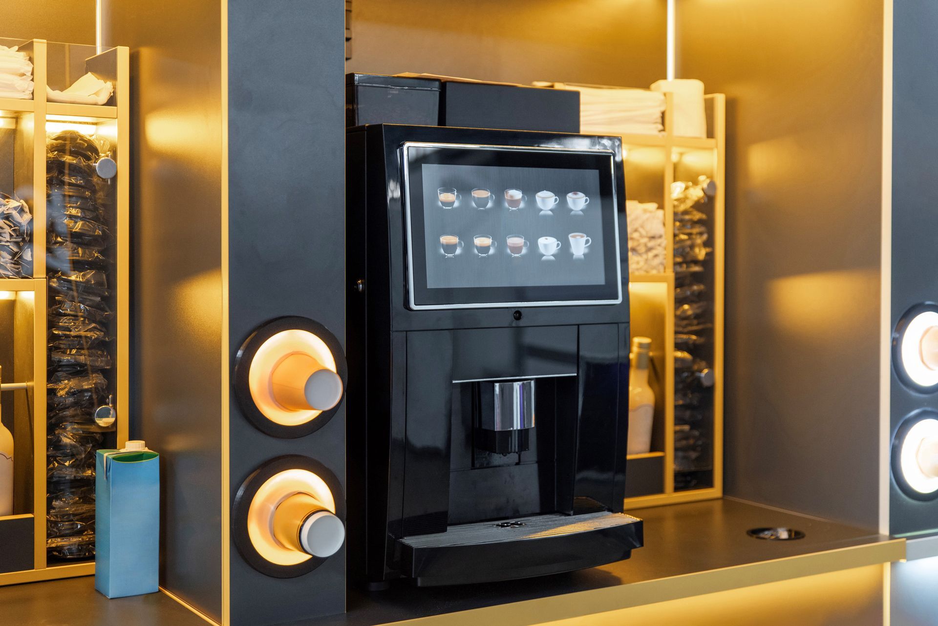 Black coffee machine with touchscreen display, integrated cup dispensers, set in a modern cafe setting.