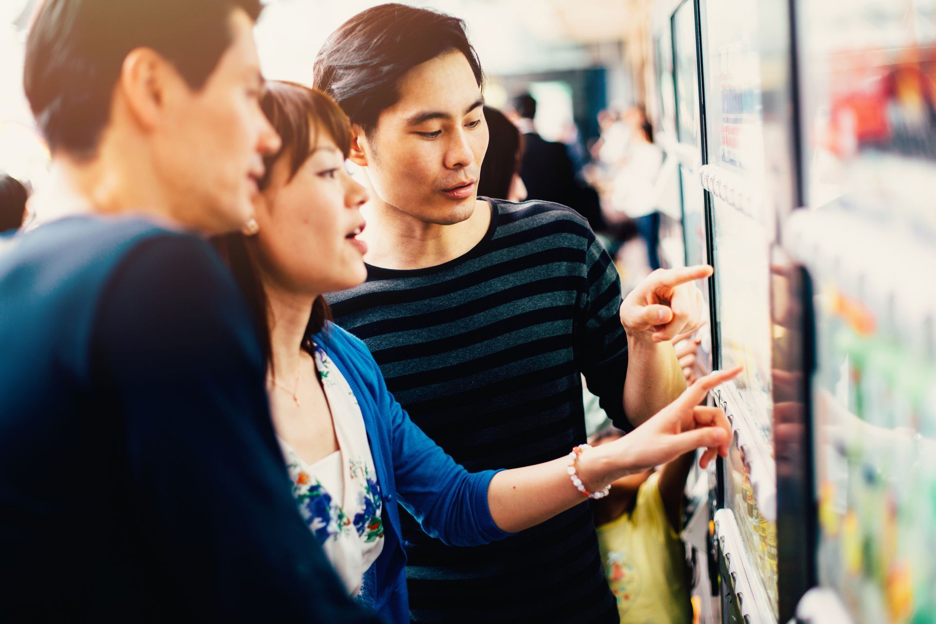 Three people looking at something on a wall, pointing. Indoors with bright sunlight.