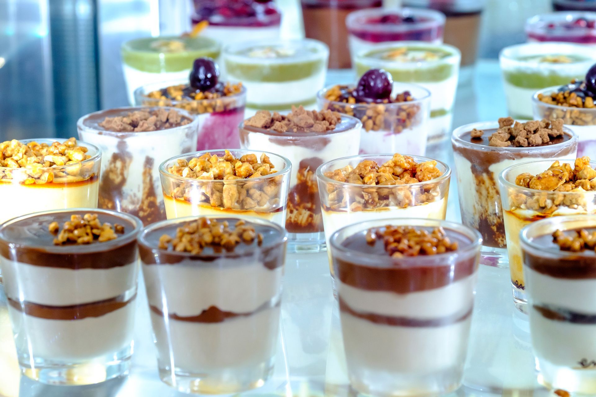 Desserts in clear glass cups on display, layers of cream, chocolate, and toppings.