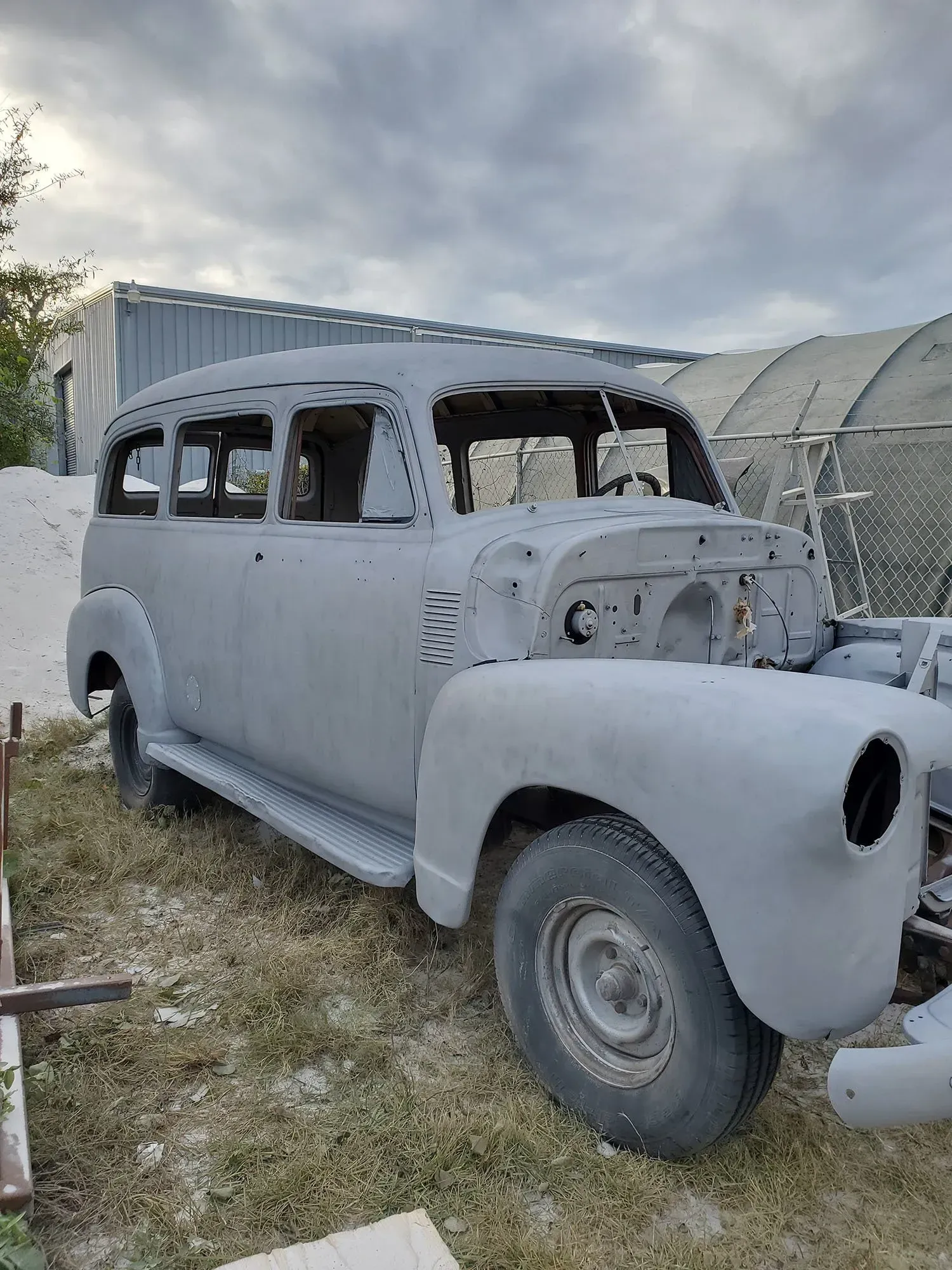 An old car is sitting in the grass in front of a building.