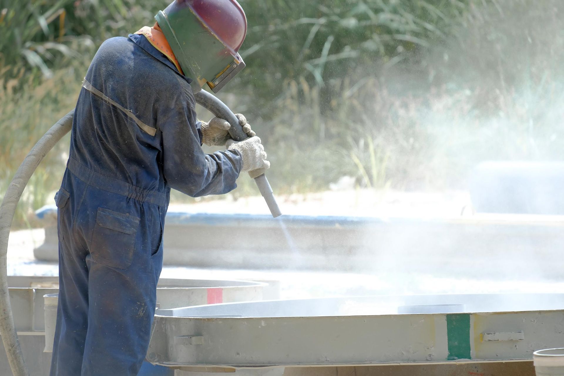 A man wearing a helmet is sandblasting a piece of wood.