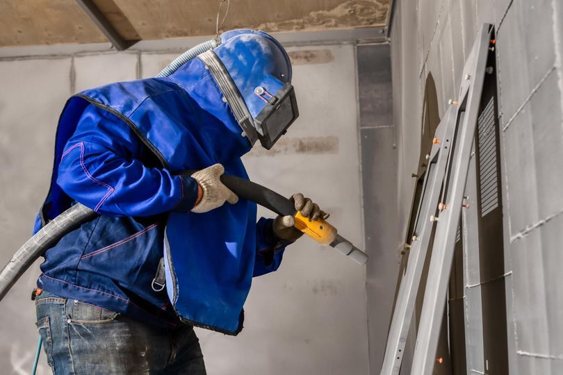 A man is sandblasting a wall with a machine.