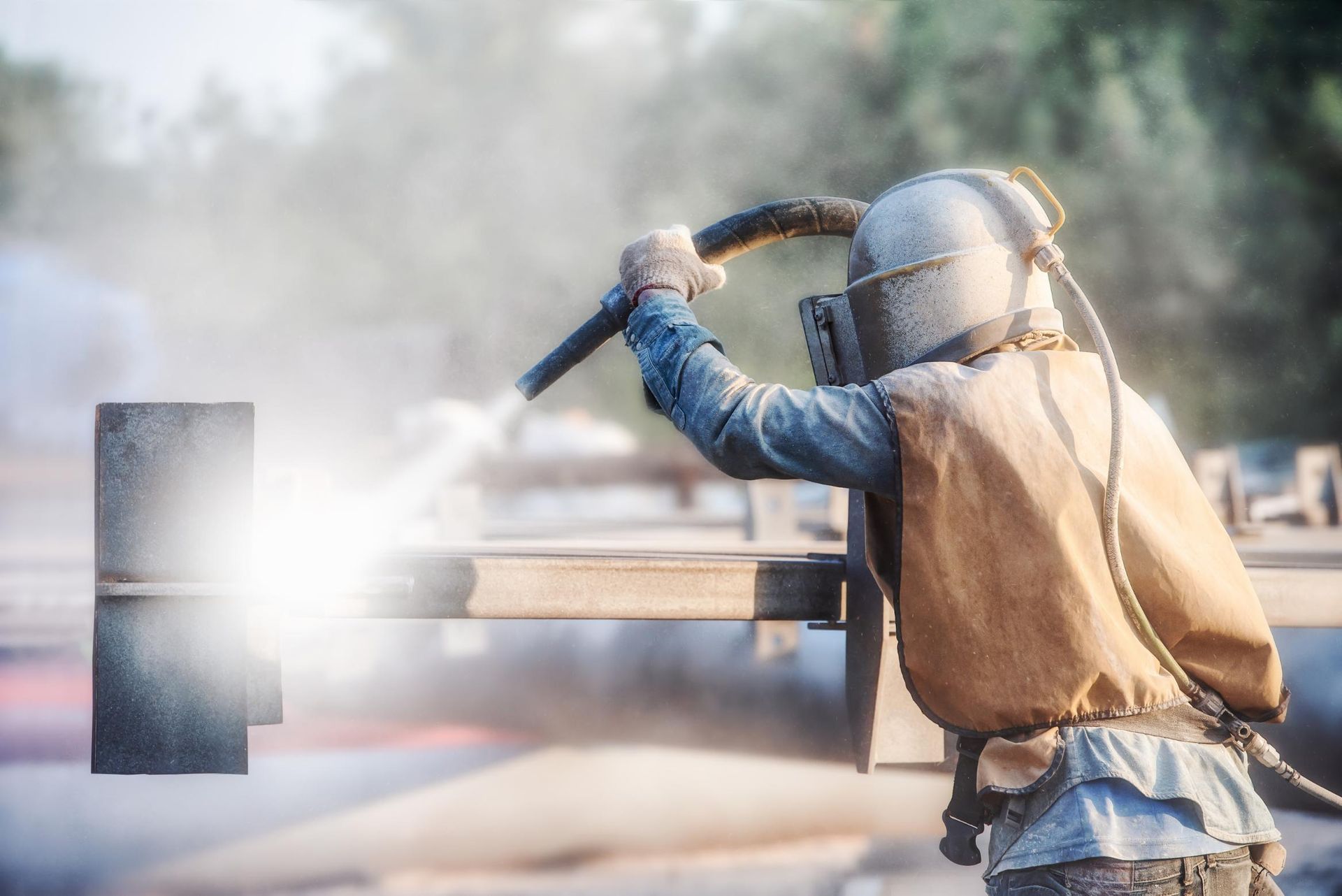 A man is sandblasting a piece of metal with a machine.