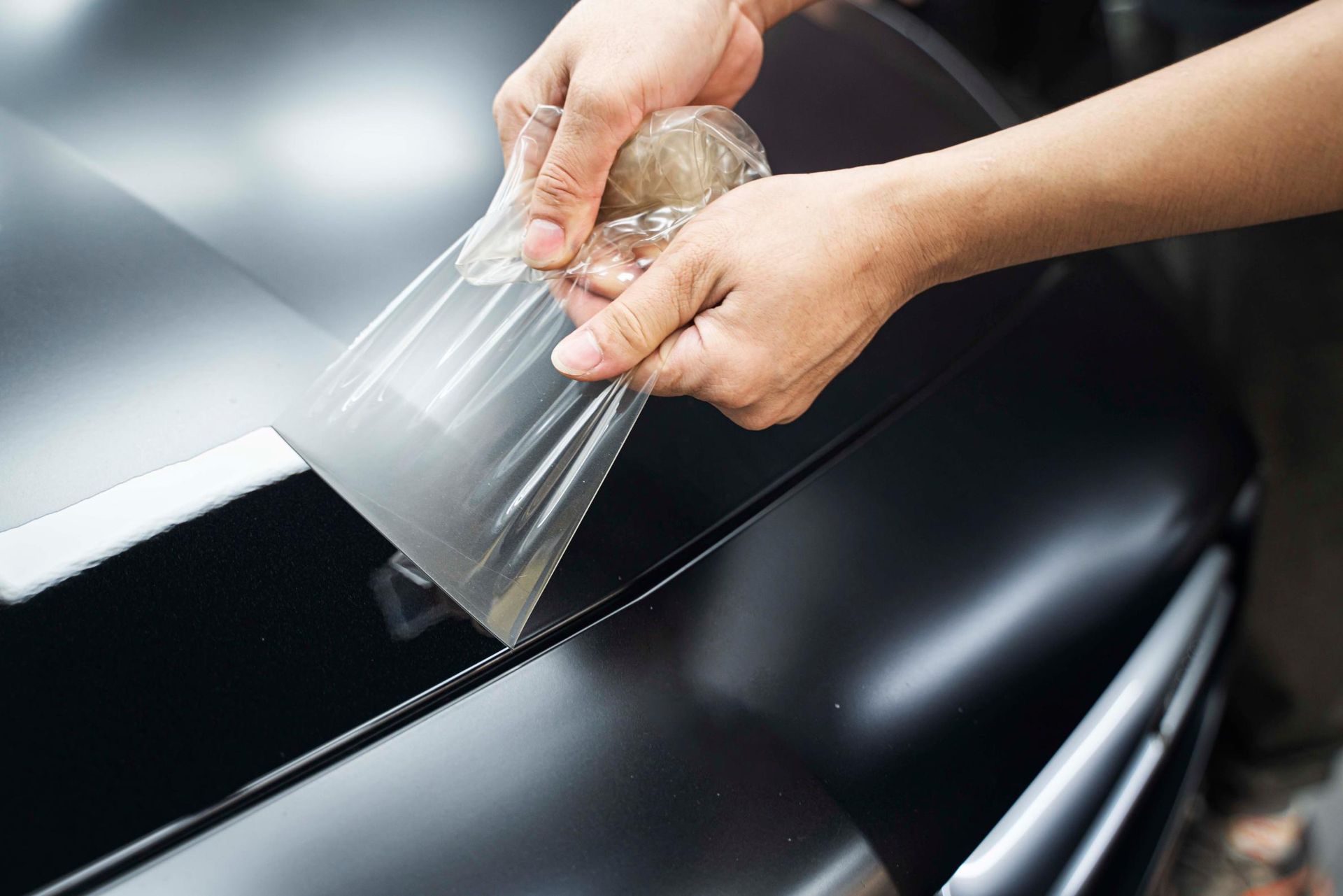 A person is applying a protective film to the hood of a car.