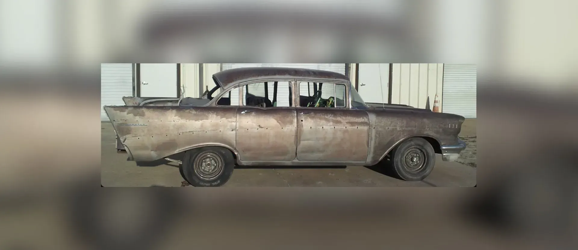 An old rusty car is parked in the dirt in front of a building.