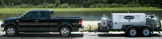 A black truck is towing a trailer with a machine attached to it.
