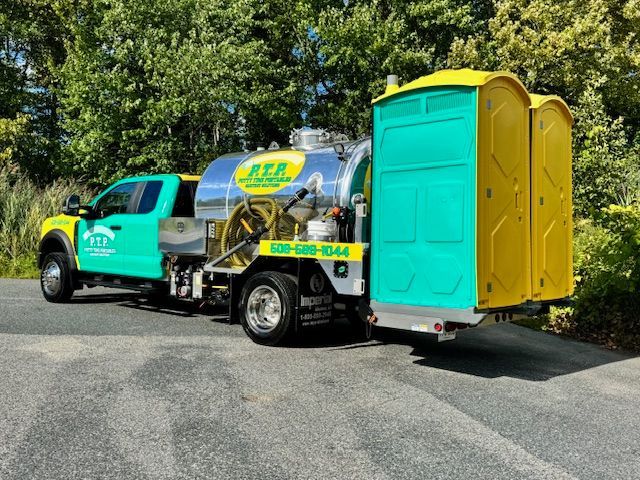 A teal and yellow truck with portable toilets attached, on a road.