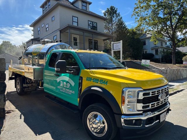 Green and yellow service truck parked in front of a house, with a large tank and logo on its side.