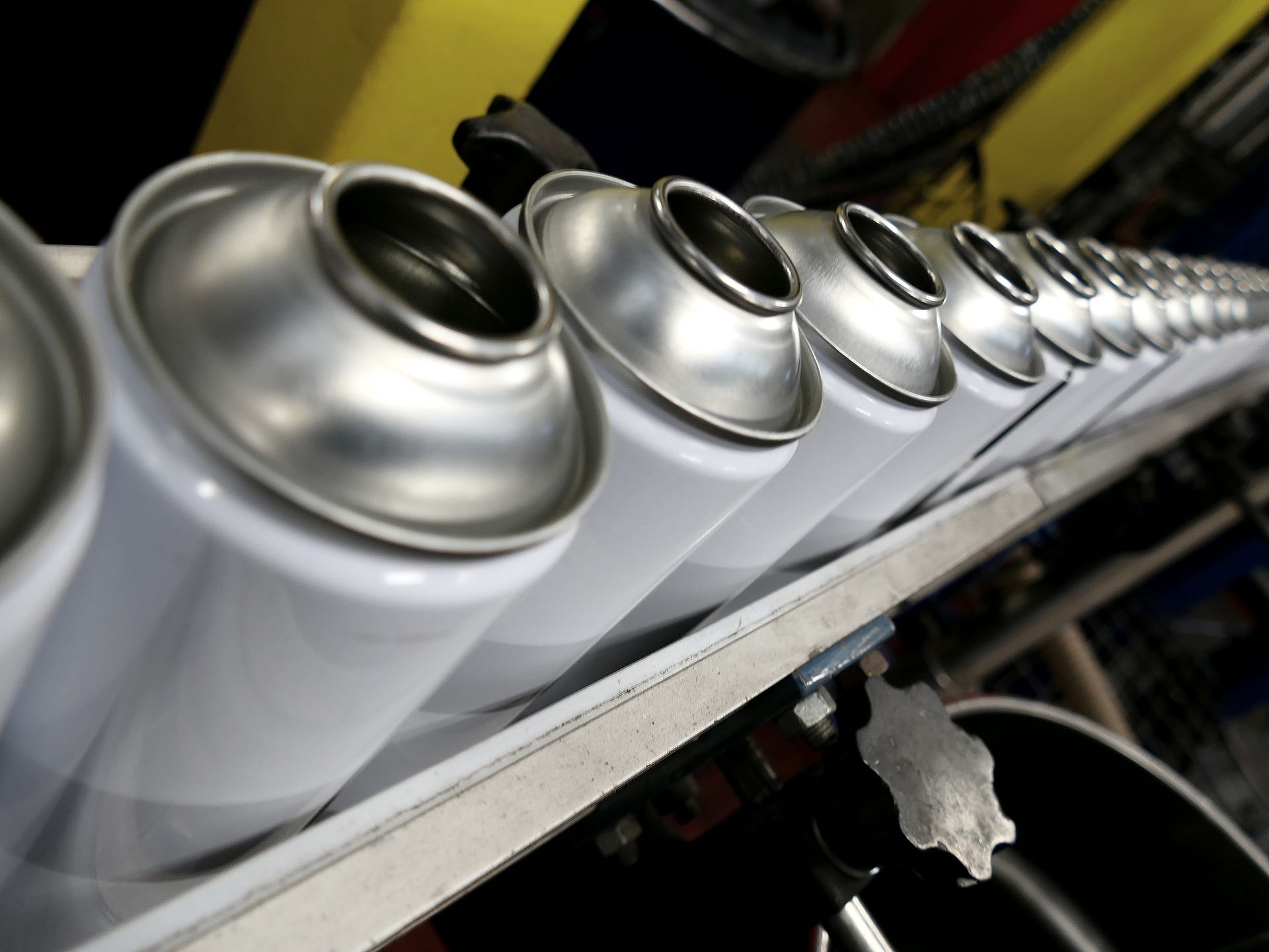 A row of empty, white aerosol canisters moves along a metal assembly line in a factory.