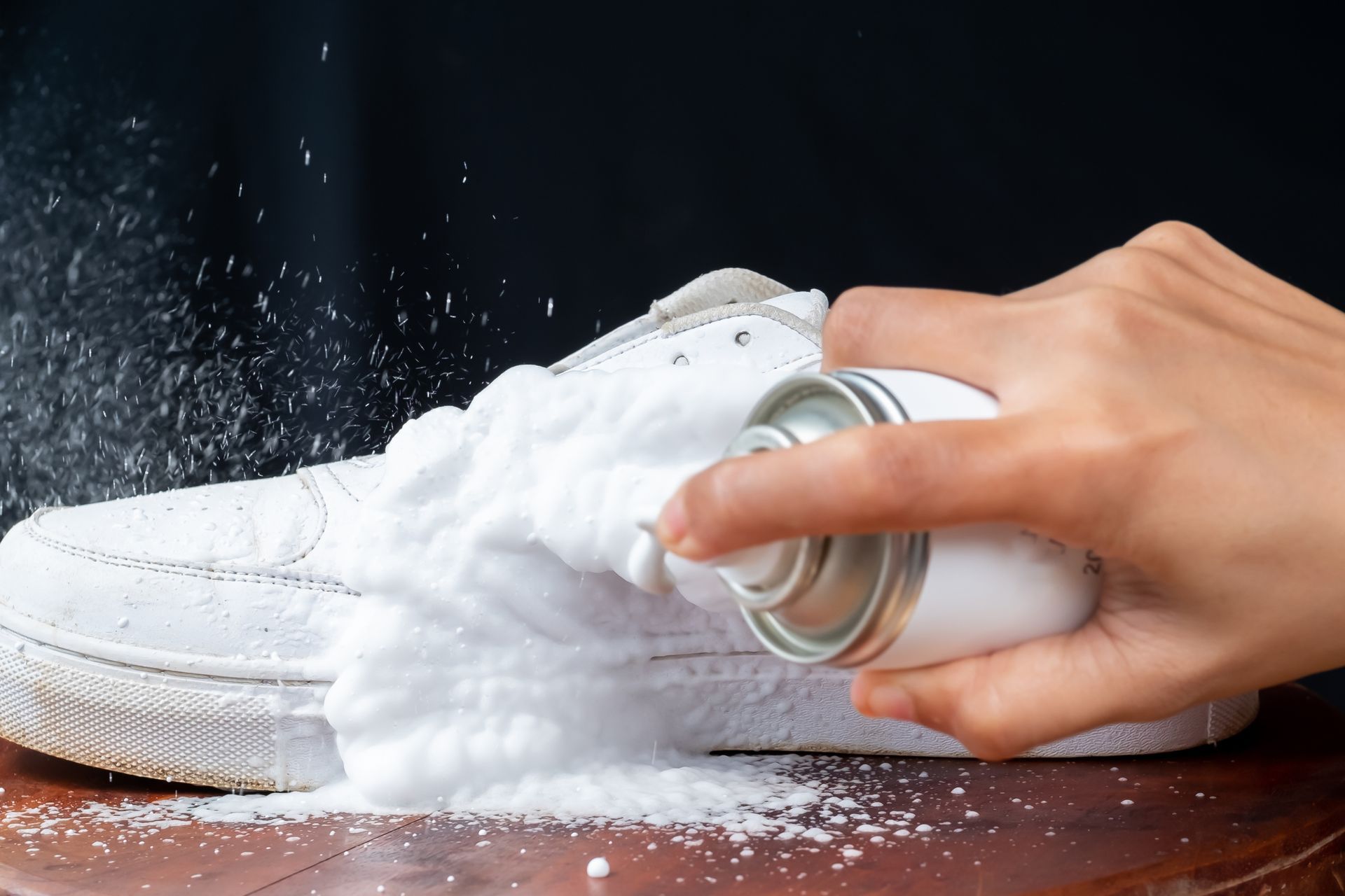 A person is cleaning a white shoe with a spray bottle.