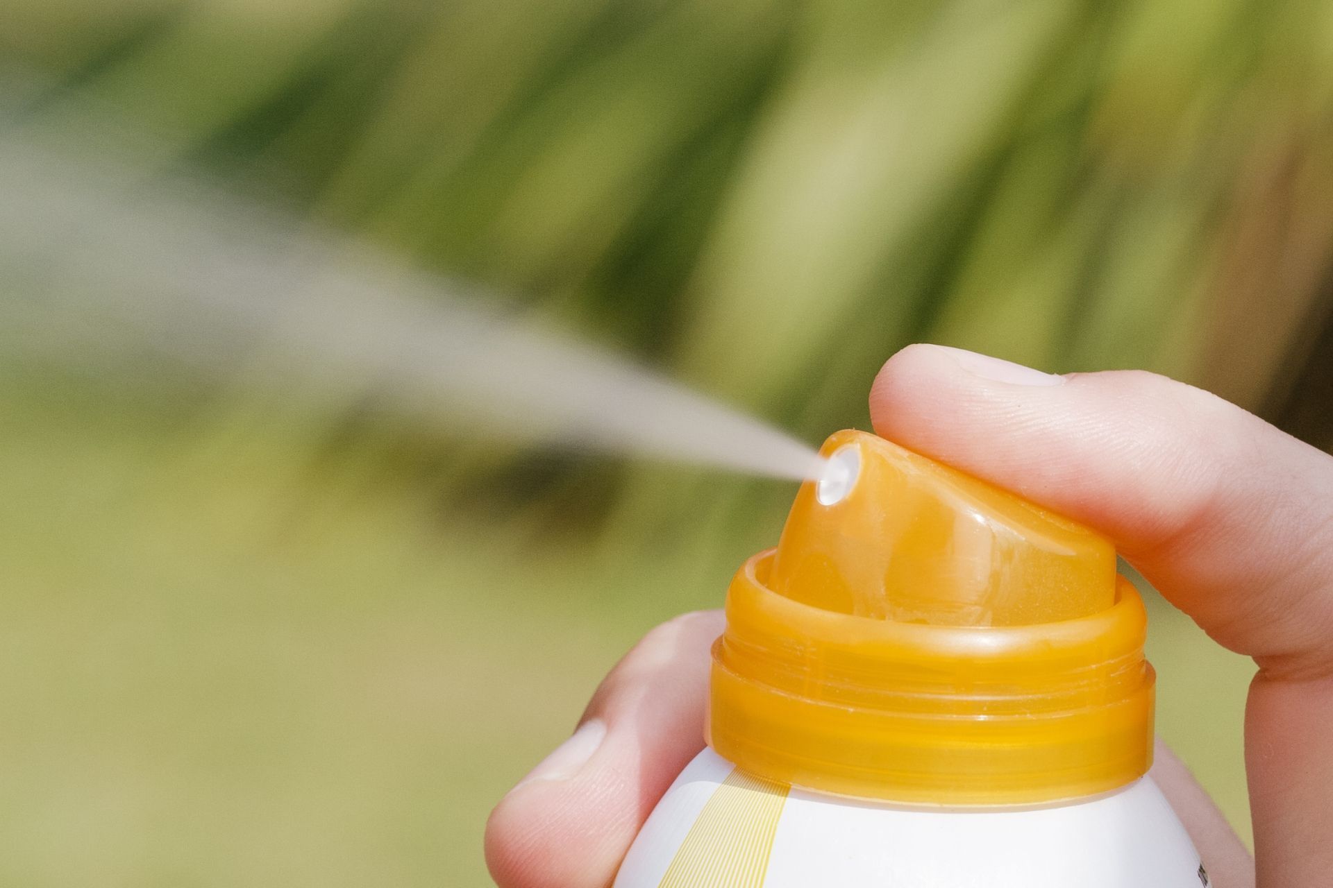 A person is spraying a bottle of sunscreen on their face.