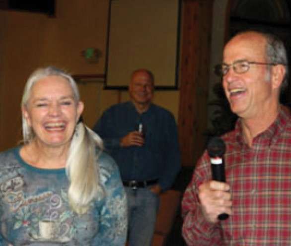 A man in a plaid shirt is holding a microphone and smiling