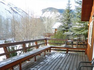 A wooden deck with a bench and chairs and mountains in the background