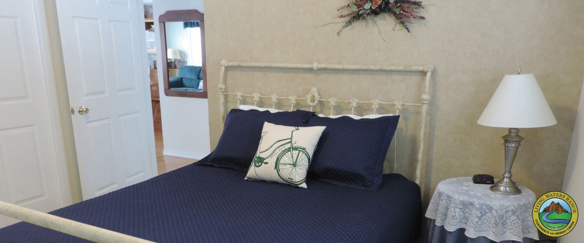 A bedroom with a bed , nightstand , lamp and mirror.