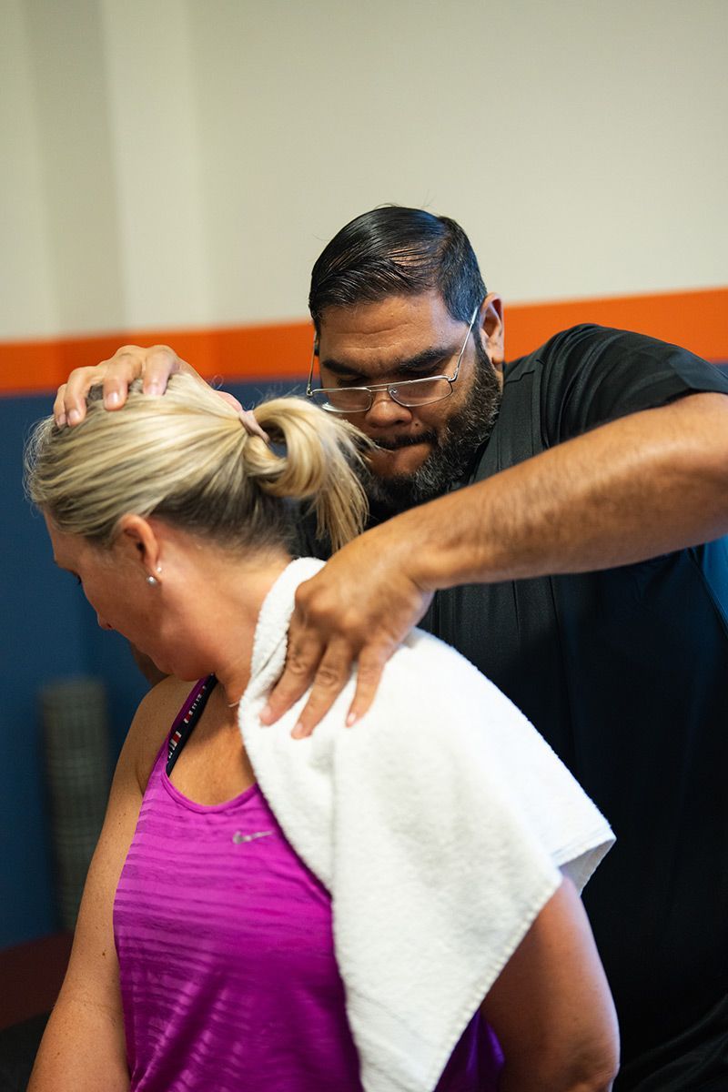 Man giving a shoulder massage to a woman in a pink top and white towel in an indoor setting