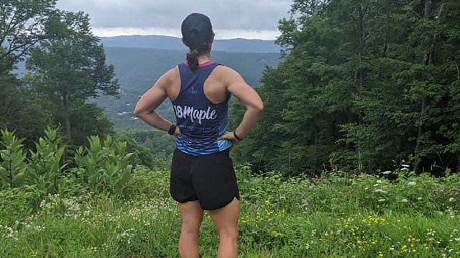 Person standing on a trail overlooking a forested mountain valley with hands on hips