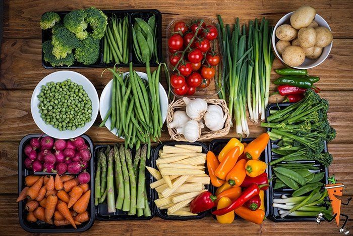 Assorted fresh vegetables arranged in baskets and crates on a wooden table.