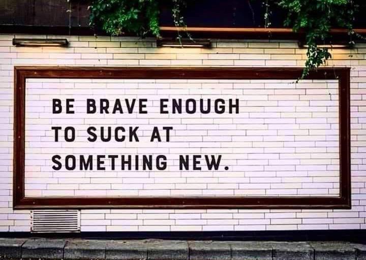 Framed sign on a brick wall reads, “Be brave enough to suck at something new.”