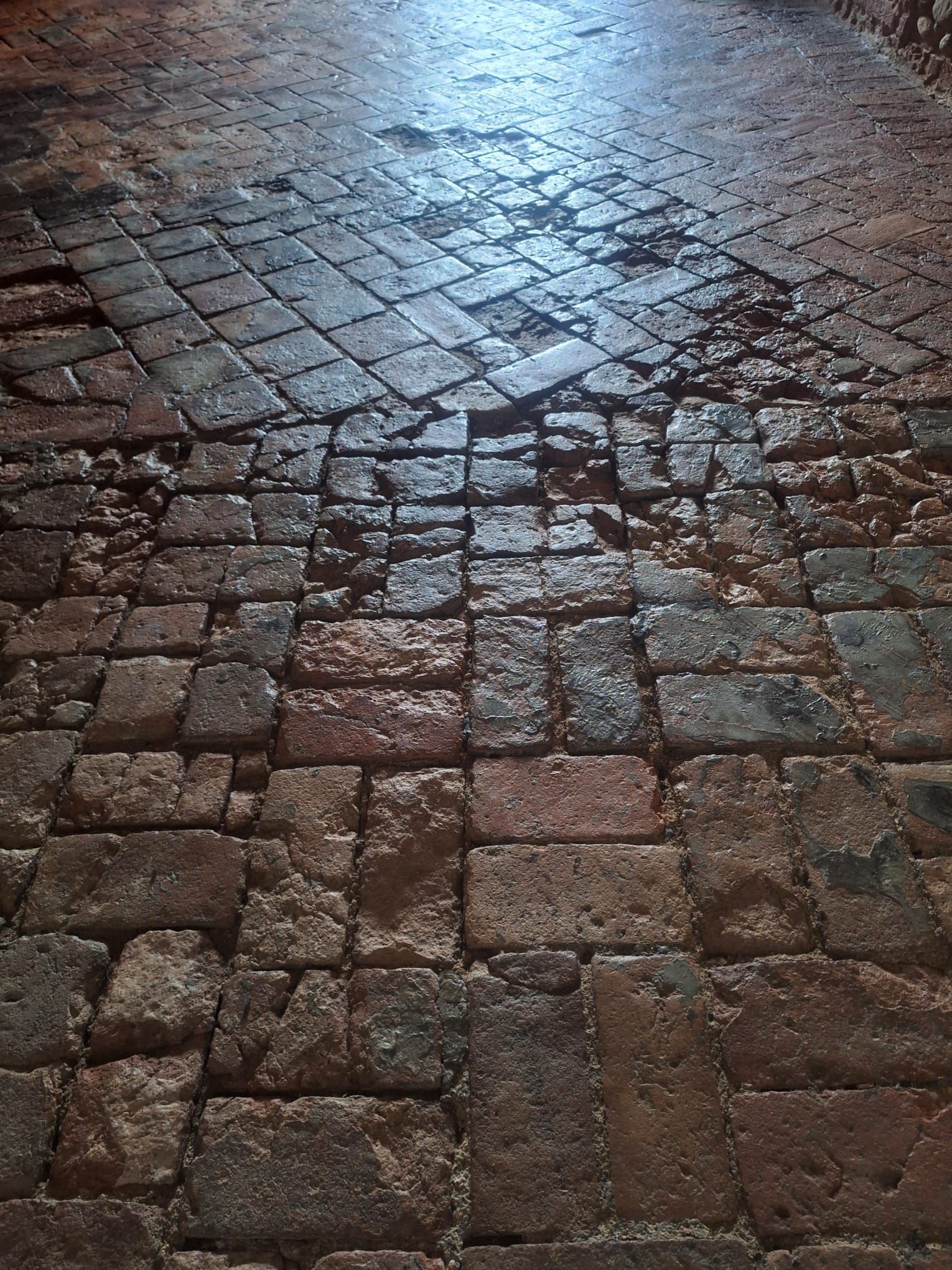 Piastrelle di pietra lucide e rettangolari disposte a formare un motivo a pavimento, che riflettono la luce.