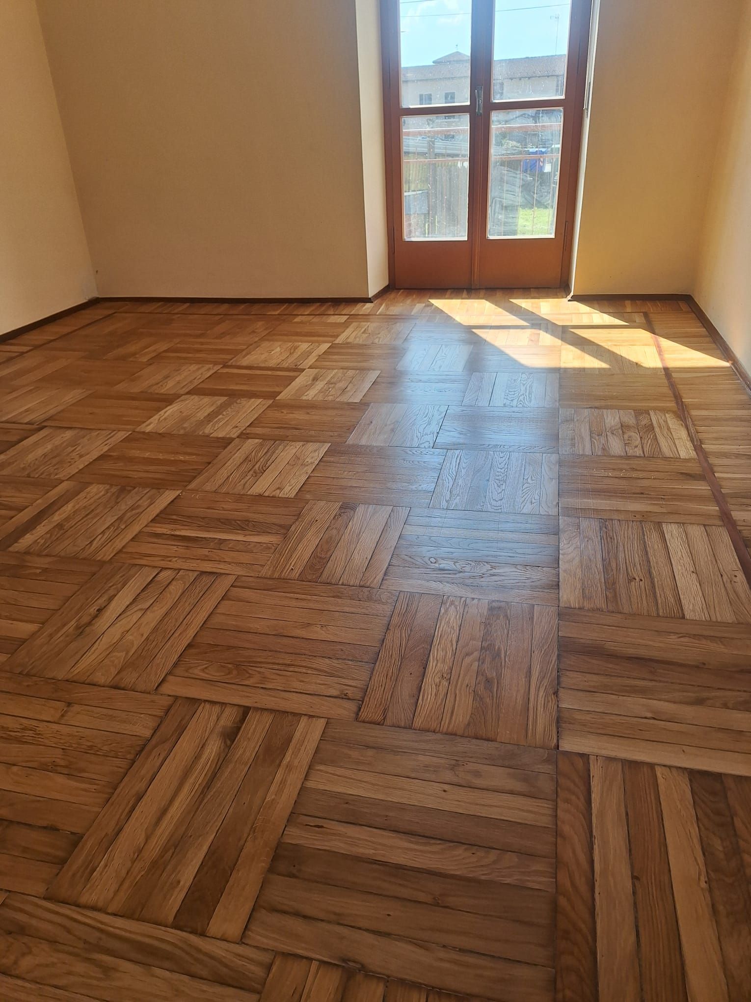 Un pennello che applica una tinta su un pavimento in parquet, cambiando il colore da chiaro a scuro.