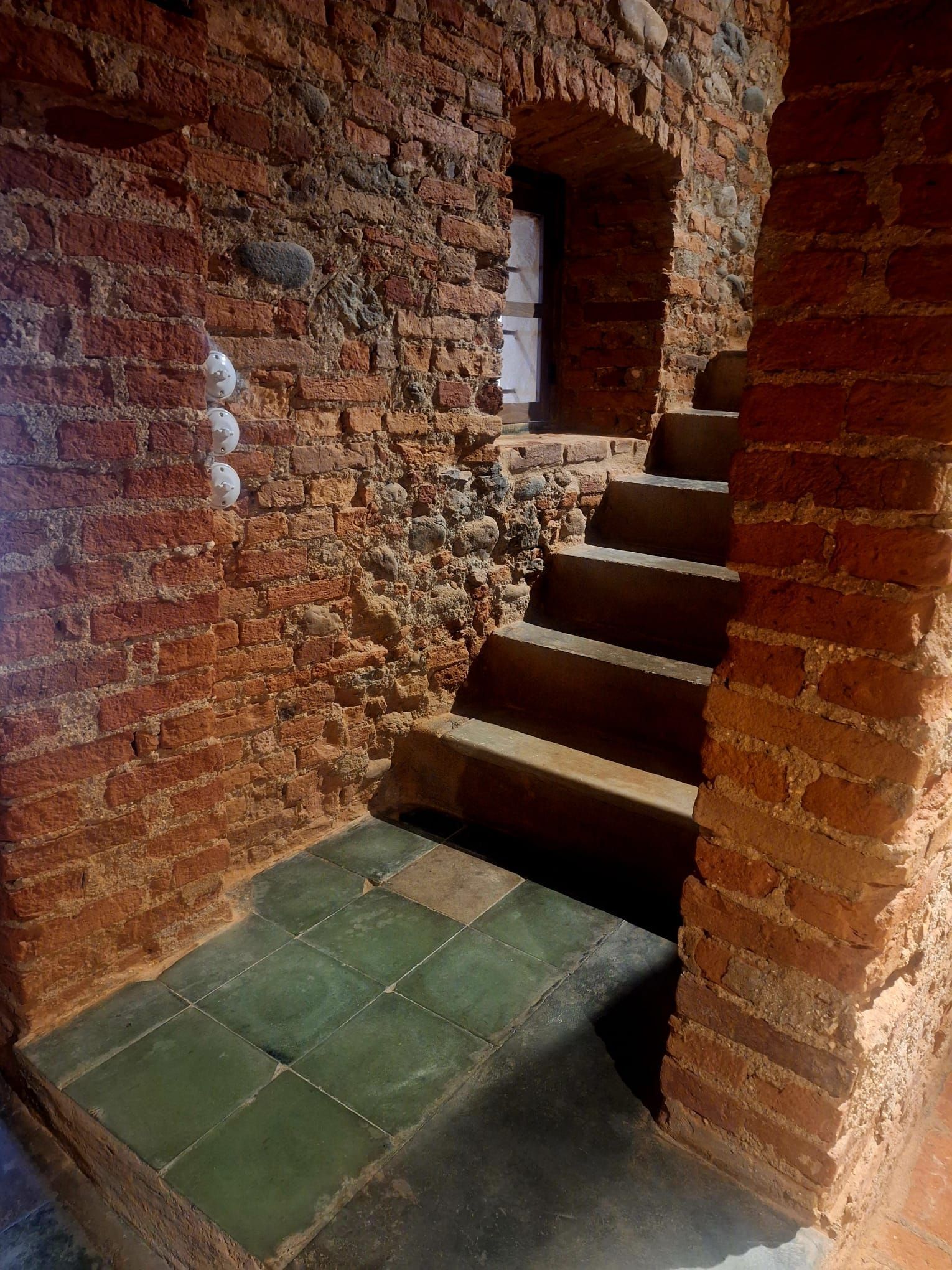 Cucina rustica con ripiani e pavimento in piastrelle rosse, pareti in pietra e mobili in legno.