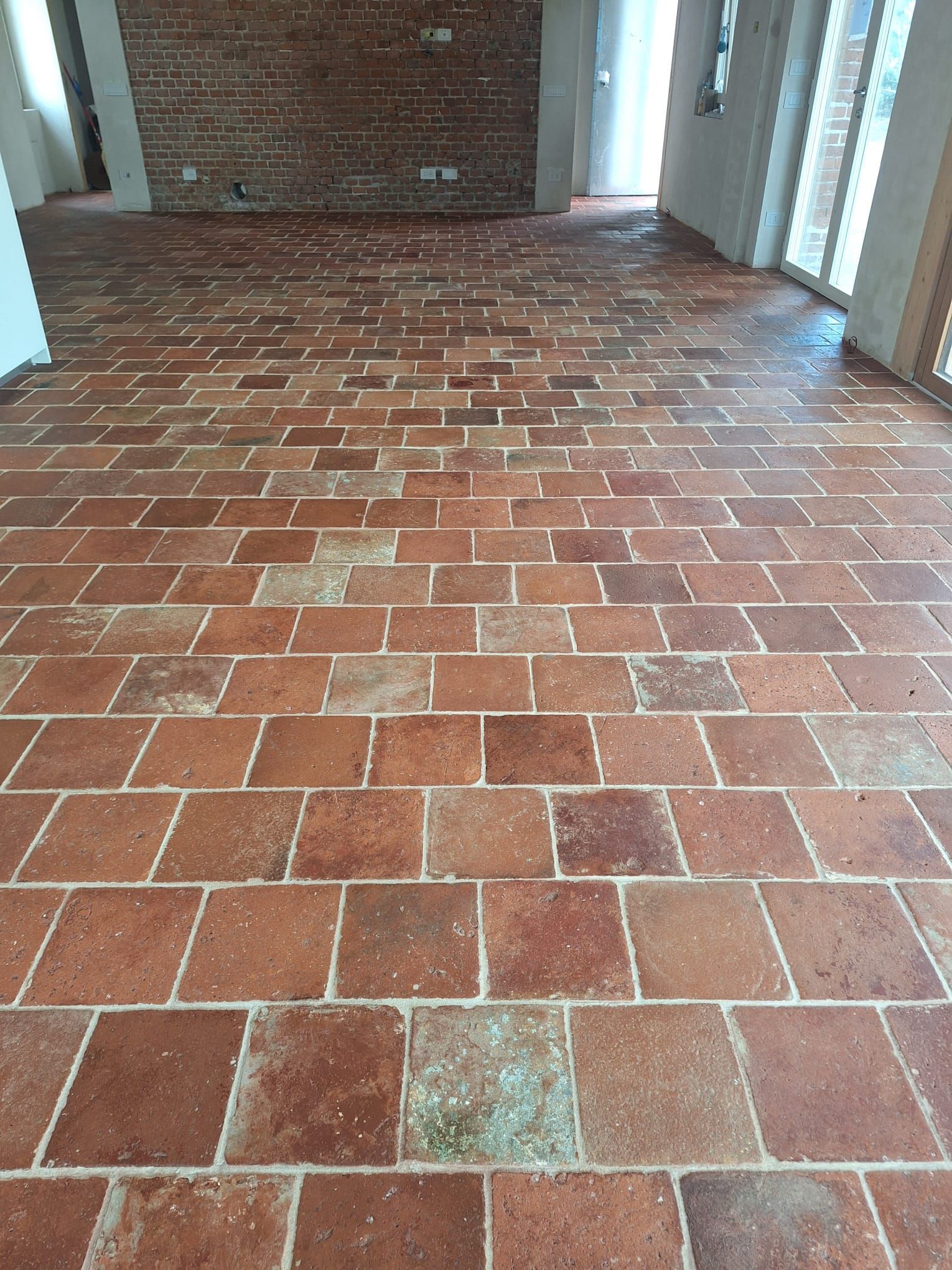 Una stanza con pavimento in piastrelle di terracotta, divano bianco, cassettiera in legno e tappeto.