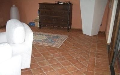 Una stanza con pavimento in piastrelle di terracotta, divano bianco, cassettiera in legno e tappeto.