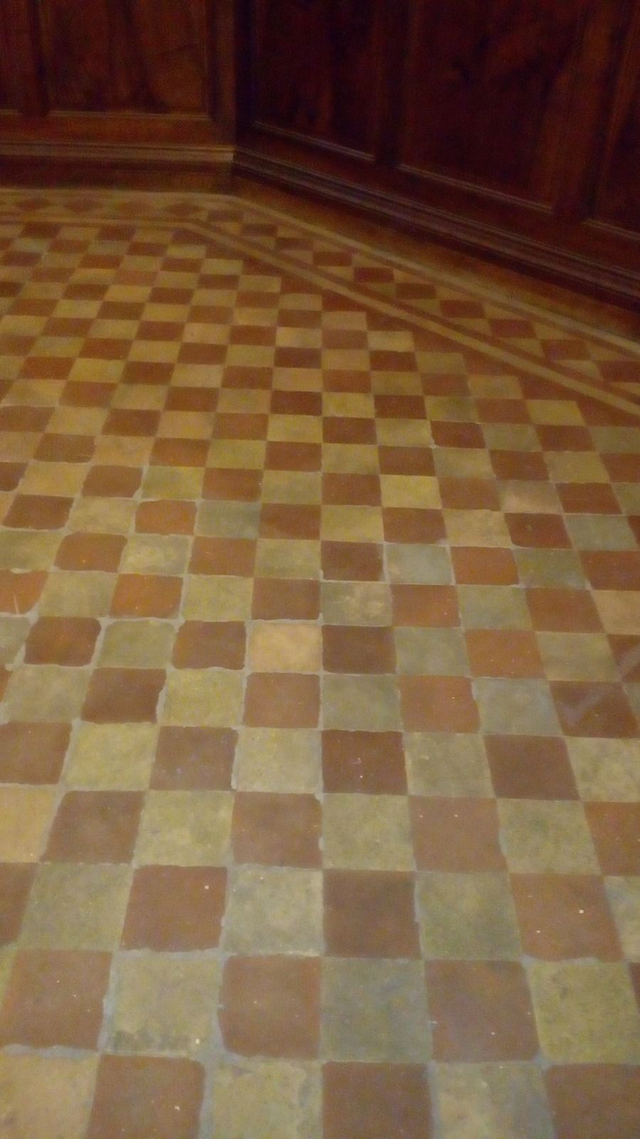 Pavimento a scacchiera con piastrelle marroni e beige e pannelli in legno sullo sfondo.