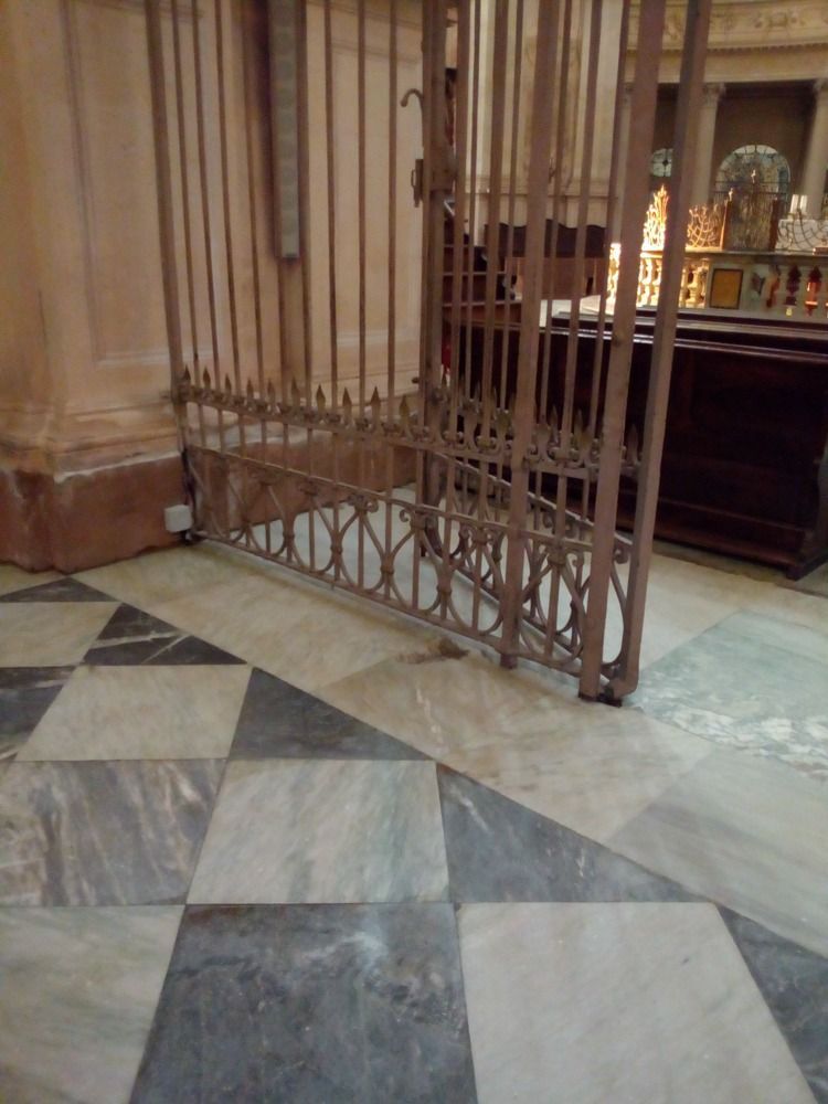 Cancello metallico socchiuso su pavimento in marmo a scacchi; interno di un edificio.