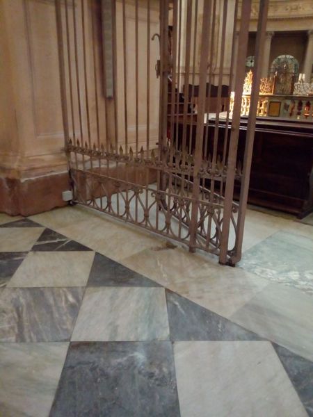 Cancello metallico socchiuso su pavimento in marmo a scacchi; interno di un edificio.