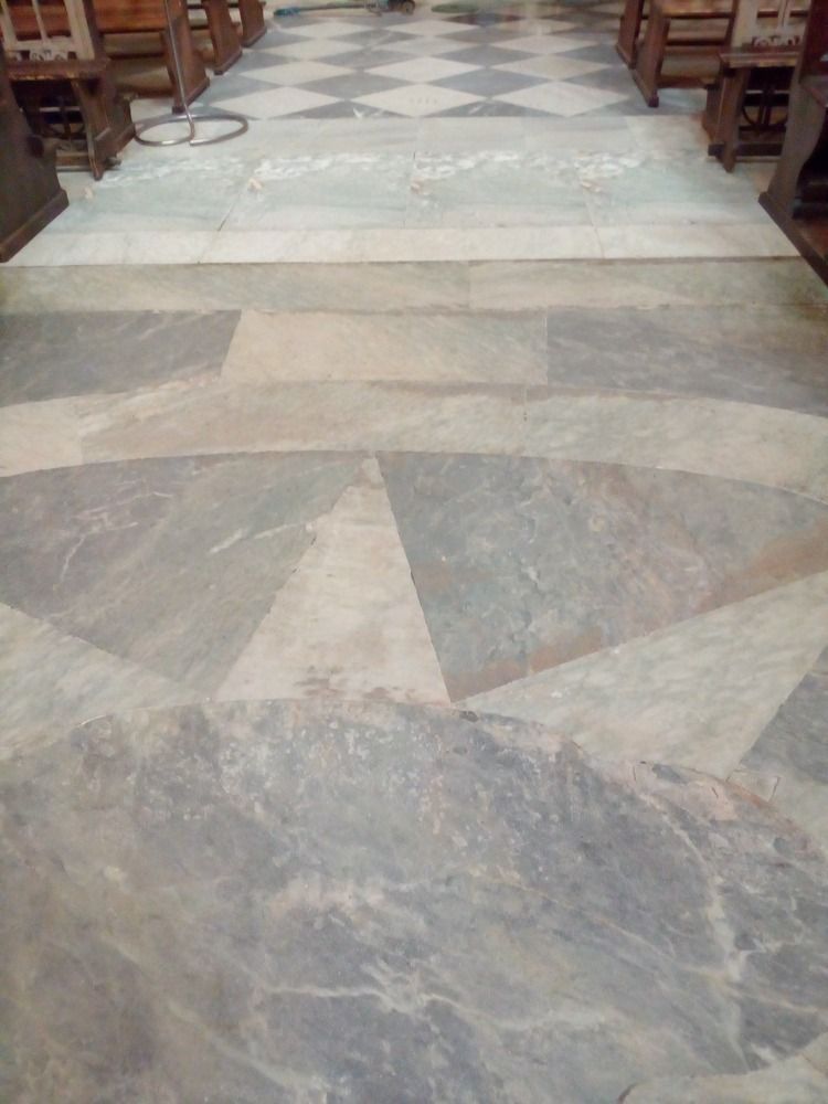 Pavimento in marmo con motivi a stelle e rombi, in una chiesa. Banchi lungo il percorso.