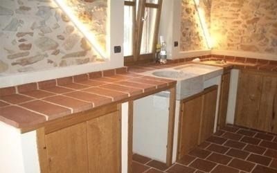 Cucina rustica con ripiani e pavimento in piastrelle rosse, pareti in pietra e mobili in legno.