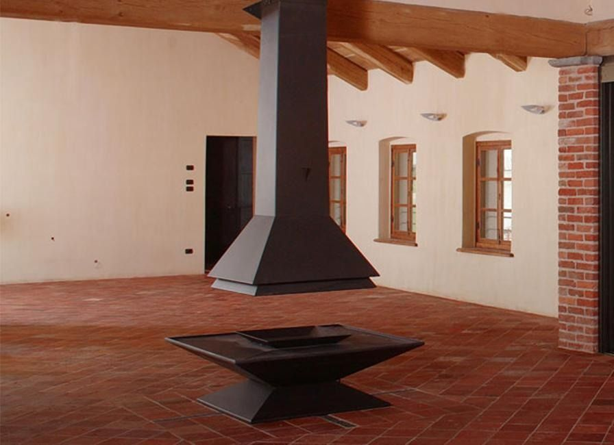 Moderno camino da interno con cappa in metallo e focolare quadrato in una stanza con pavimento in piastrelle di terracotta.