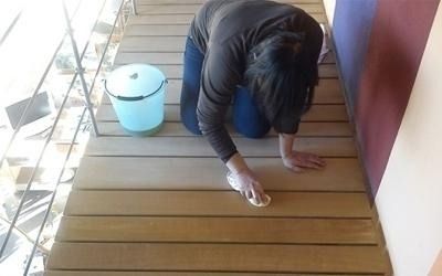 Persona inginocchiata sul pavimento di legno, intenta a pulirsi con un panno, con un secchio nelle vicinanze.