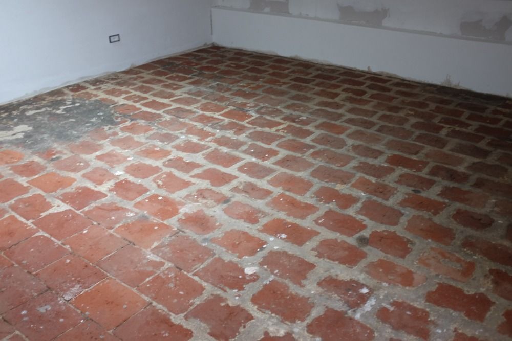 Pavimento in mattoni rossi in un angolo di una stanza, con stucco visibile tra i mattoni.