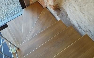 Scala a chiocciola in legno che sale, con un muro di mattoni e una ringhiera in metallo.