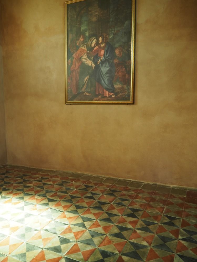 Dipinto su una parete dai toni caldi su un pavimento in piastrelle; la luce proveniente dalla finestra illumina il pavimento.