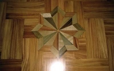 Pavimento in legno con intarsio a forma di stella in diverse tonalità di legno.
