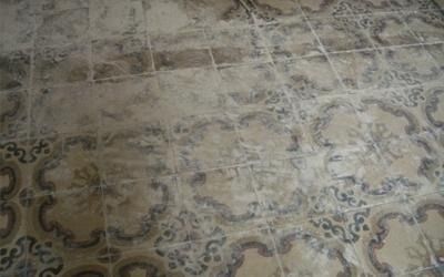 Pavimento piastrellato con motivo floreale sbiadito, color marrone chiaro e scuro con contorni neri.