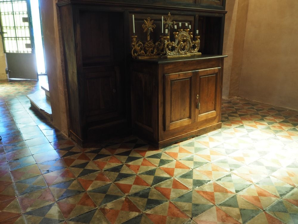 Mobiletto in legno con portacandele decorati su pavimento piastrellato. Ingresso sullo sfondo.