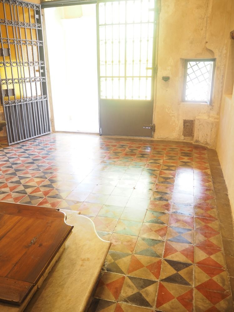 Pavimento piastrellato in una stanza con porta aperta e finestra. Le piastrelle sono rosse, nere e bianche.