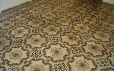 Pavimento piastrellato decorato con motivi floreali beige, marroni e dorati.