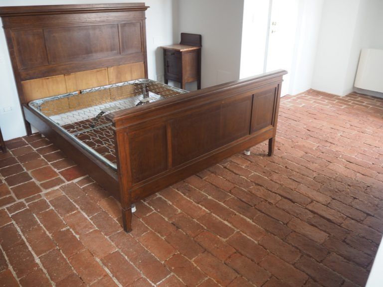 Stanza vuota con pavimento in mattoni rosso-marroni, pareti bianche e una piccola finestra.