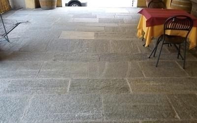 Pavimento in pietra con lastre rettangolari, tavolo con tovaglia rossa e sedia nera.