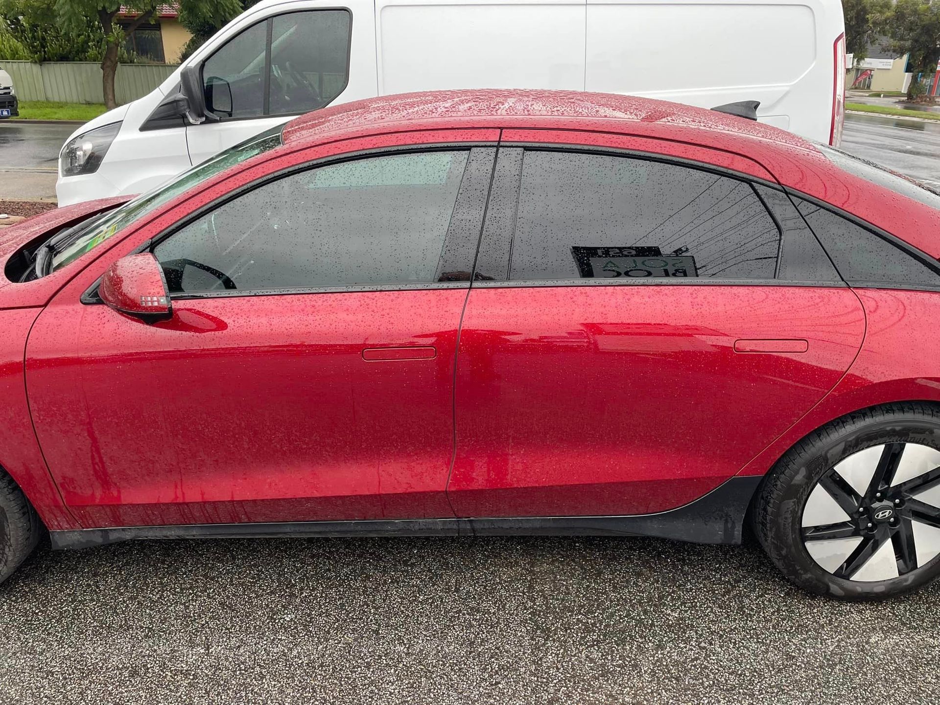 A Red Car Is Parked Next To A White Van In A Parking Lot – Adelaide, SA - Sola Bloc Window Tinting